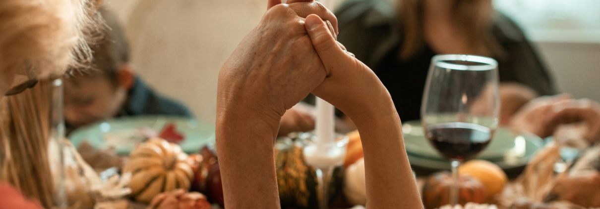 A family holding hands in prayer before a Thanksgiving dinner indoors with warm fall decor.